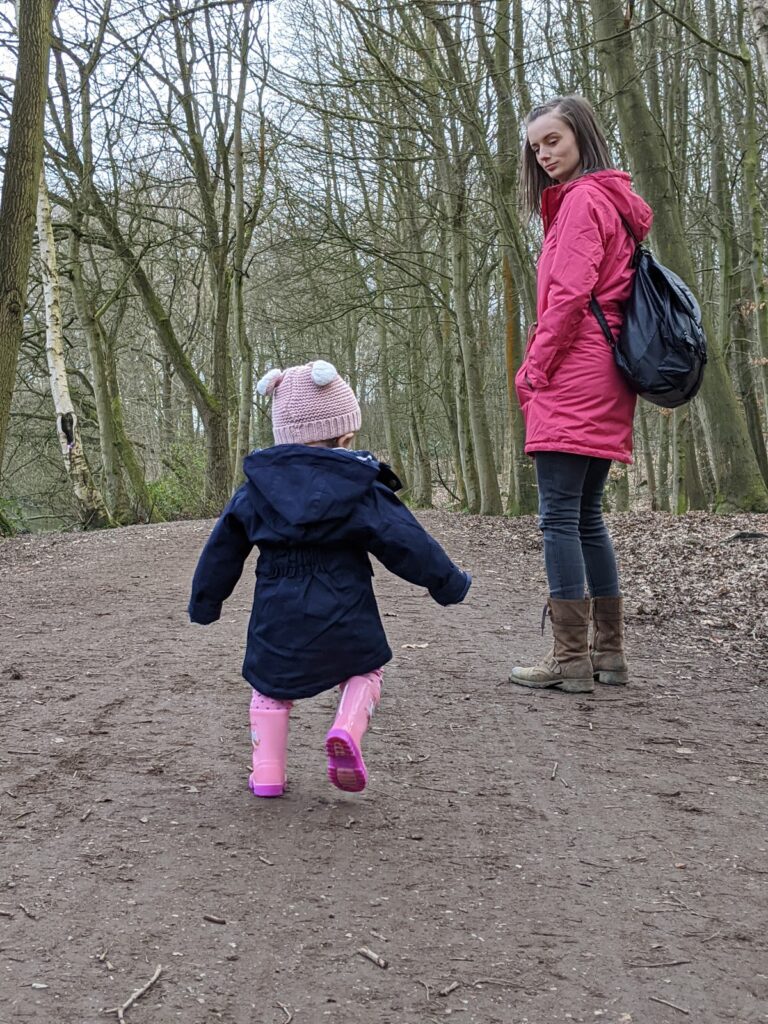 Back shot of toddler walking through woodland scene wearing Lighthouse navy raincoat. Woodland walks with Lighthouse Clothing.