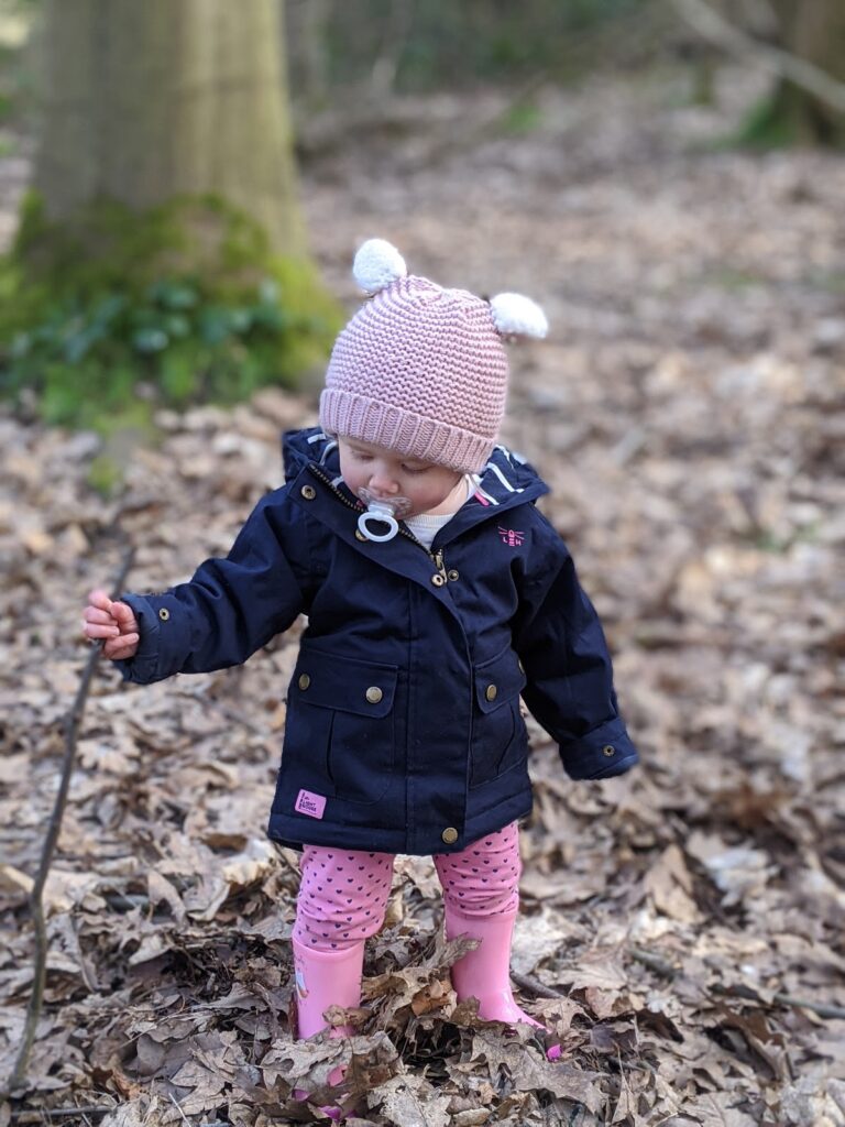 Woodland walks with Lighthouse Clothing. Toddler wearing navy Lighthouse raincoat with pink bobble hat.