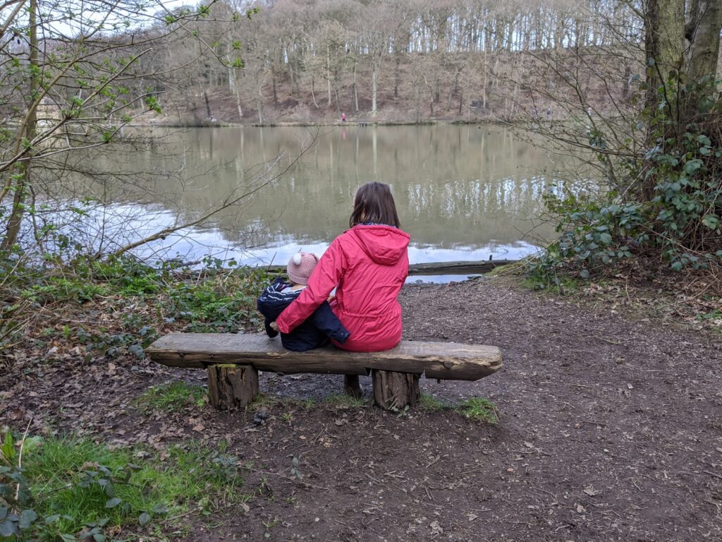 Woodland walks with Lighthouse Clothing. Back shot of mother and daughter wearing Lighthouse raincoats looking out onto woodland lake.