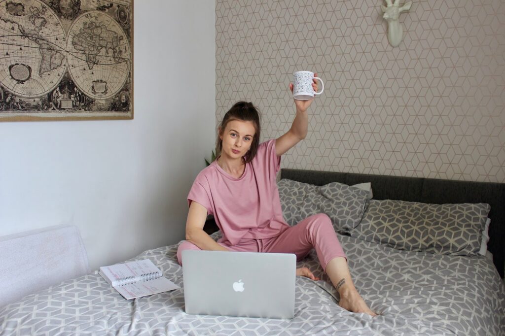 Claire sat on bed in loungewear with a cup of tea in front of her laptop. Positive highlights from 2020.