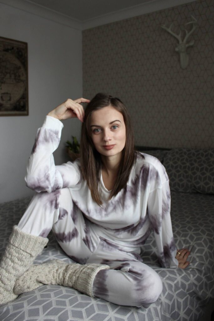 Claire sat cross legged on the bed wearing Femme Luxe tie dye loungewear set. How to give mum guilt the middle finger.