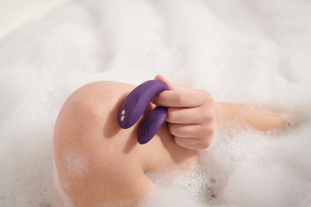 Woman holding sex toy in bubble bath.