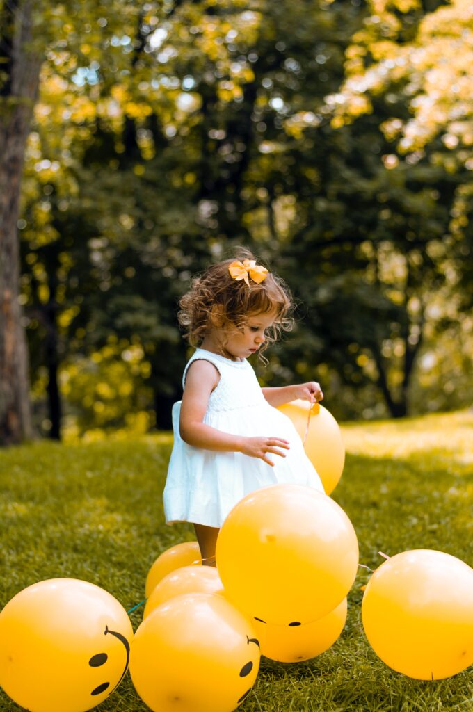 Toddler girl surrounded by smiling face balloons. Tips on raising a respectful child.