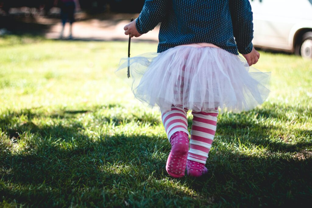 How to keep your child safe when learning to walk. A toddler walking away from the camera wearing a tutu and striped leggings.