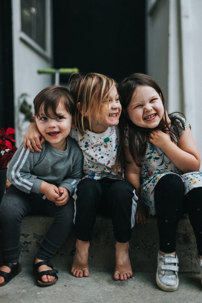 Three children sitting happily together. This post features tips on how to raise a compassionate child.