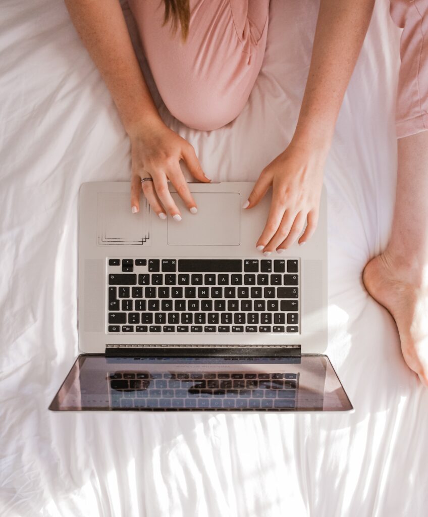 Woman sat at laptop on the bed.