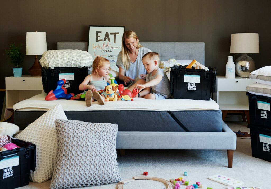 Moving house with a baby. Iage of mother on bed with kids surrounded by moving boxes.
