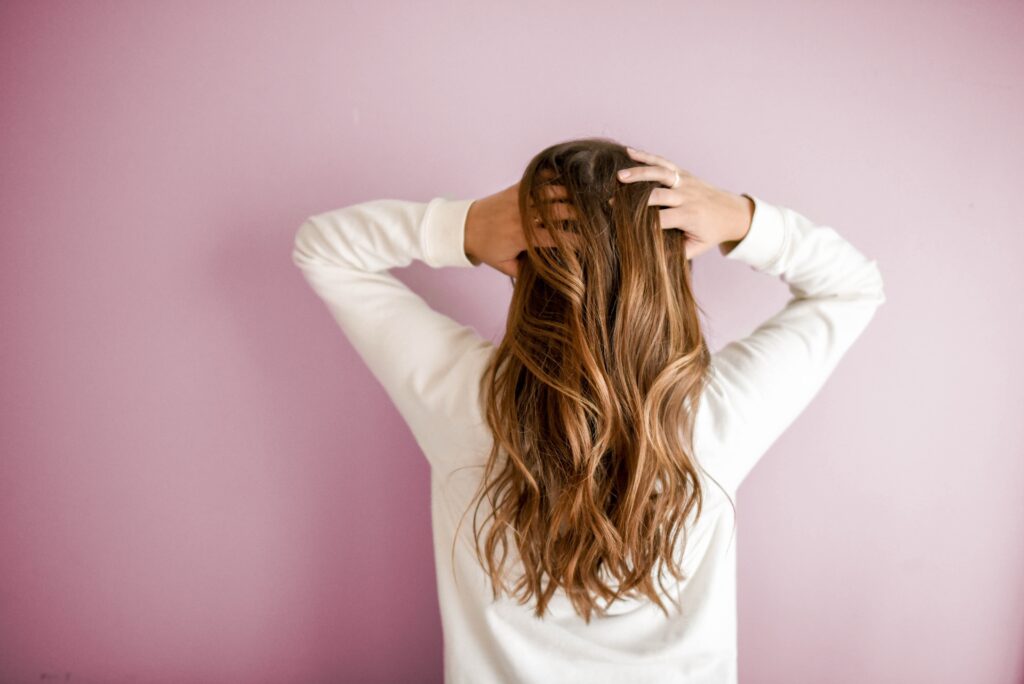 Woman facing away running her hands through her long healthy shiny hair.