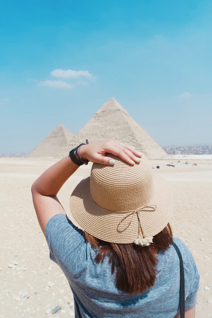 Image of woman holding onto her hat looking towards the Egyptian pyramids. This post is how to best prepare for your Sharm El Sheikh holiday.
