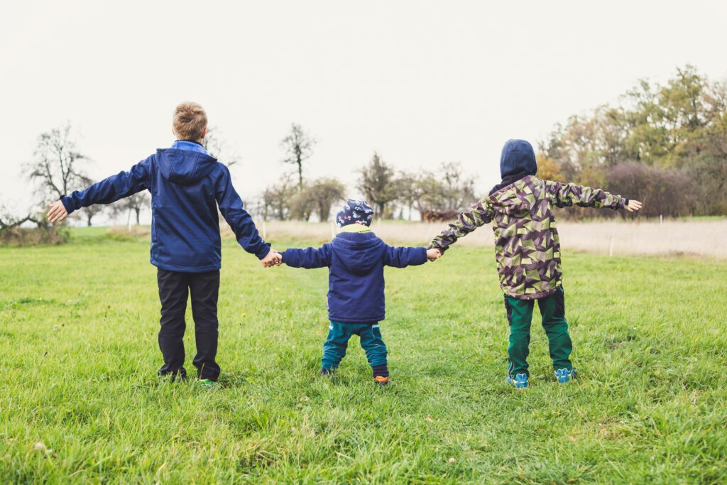 Three children holding hands. Encouraging a strong sibling bond is so beneficial. This blog post gives you five tips to help do so.