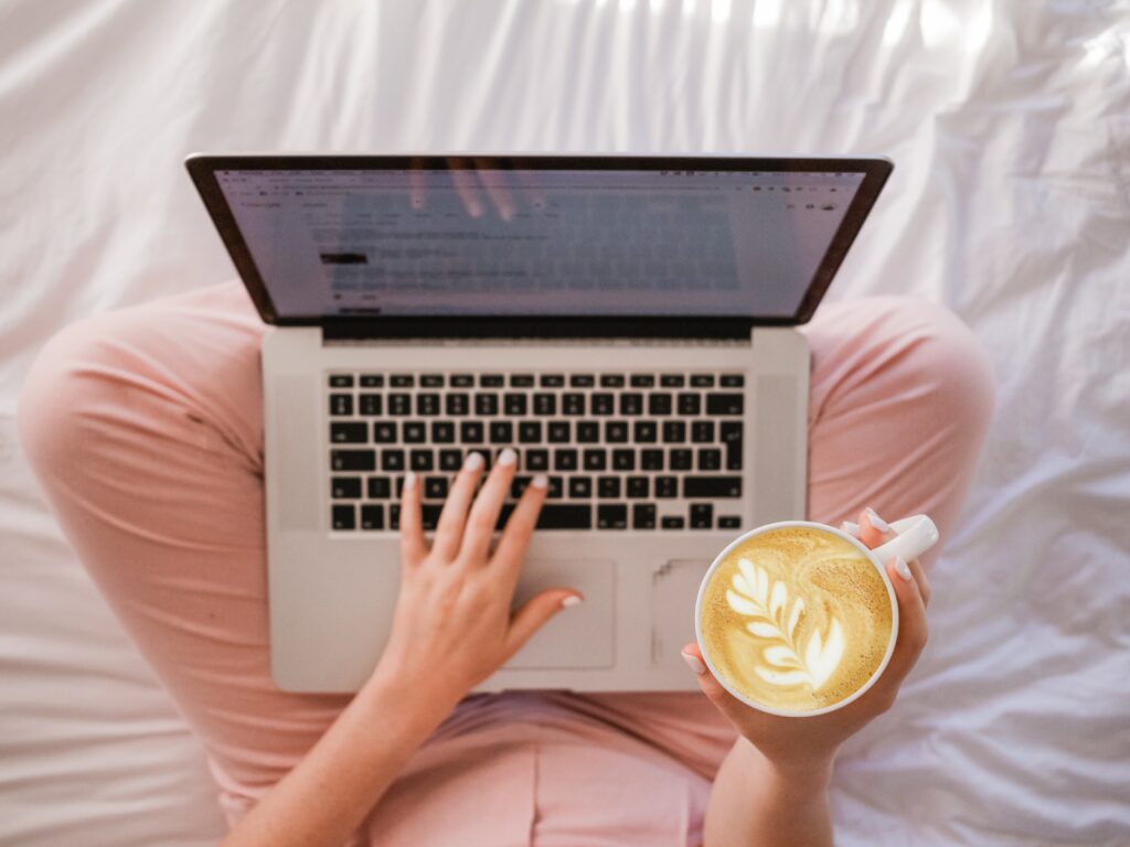 Woman sat at laptop holding a coffee. This is for a blog post which discusses ways you can use ChatGTP for blogging.