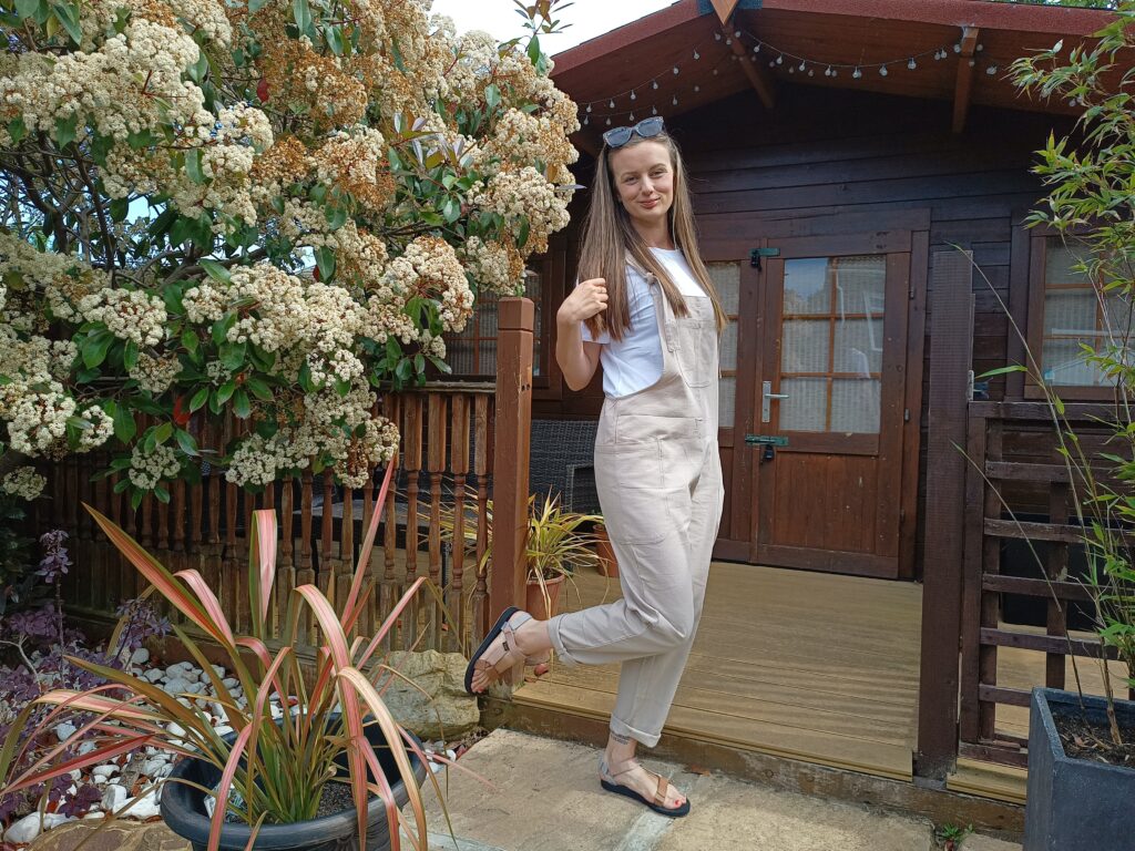 Claire Mac wearing beige dungarees white tee and sandy coloured teva sandals.
