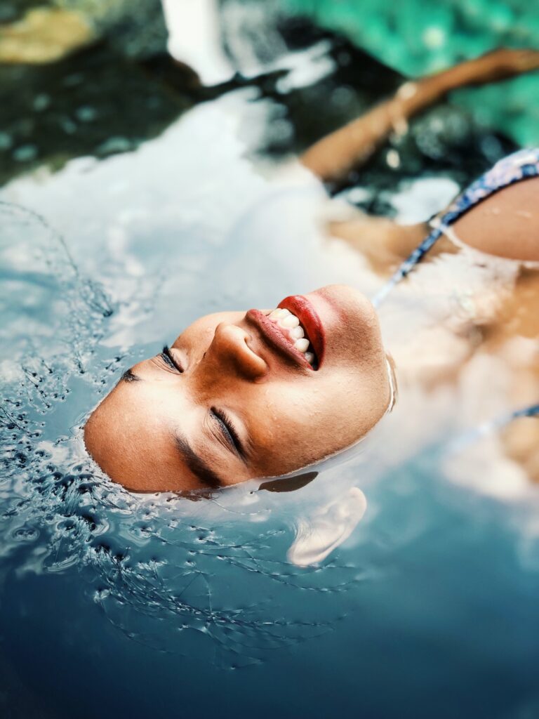 Editorial shot of woman floating on her back in water. This is to go with an article discussing ways to keep your skin healthy in summer.