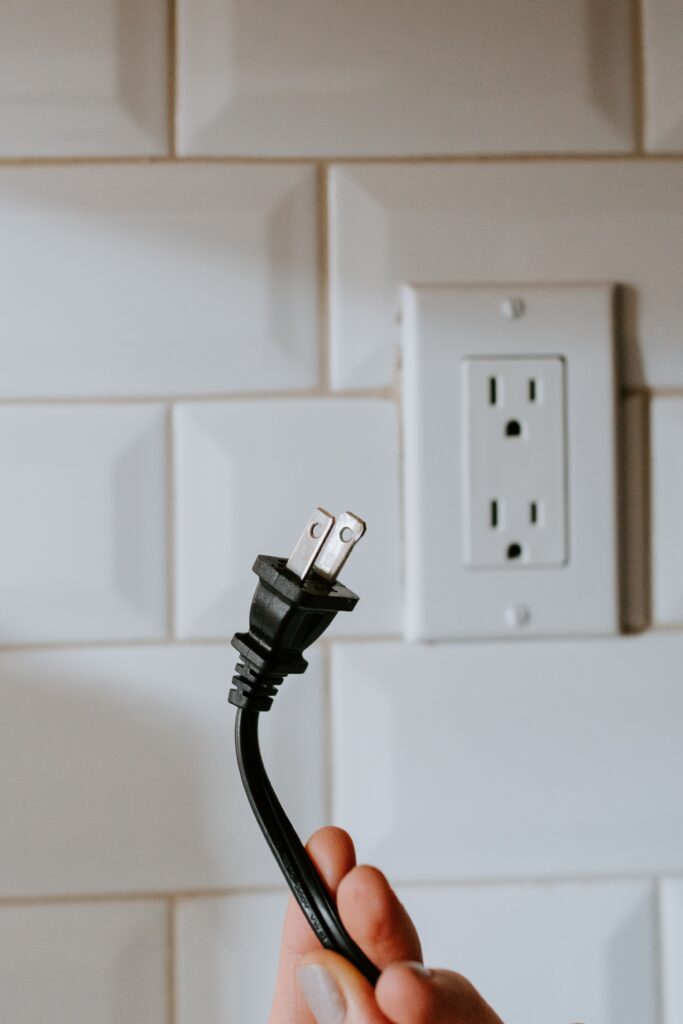 Hand holding electrical wires and plug socket. This is for a blog post detailing at home tips for electrical repairs.