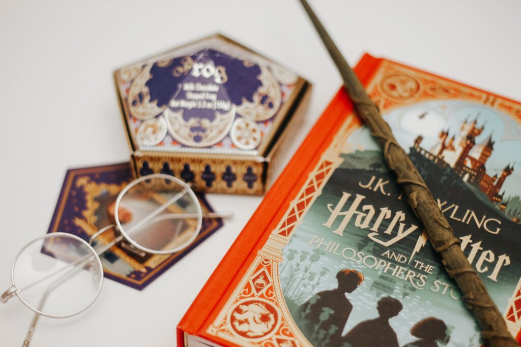 Fantasy style set up of Harry Potter and the philosophers stone book along with glasses and chocolate frog.