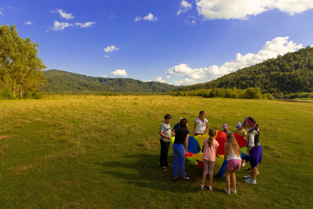 Group of children developing social skills in an outdoor setting, playing with rainbow parachute.
