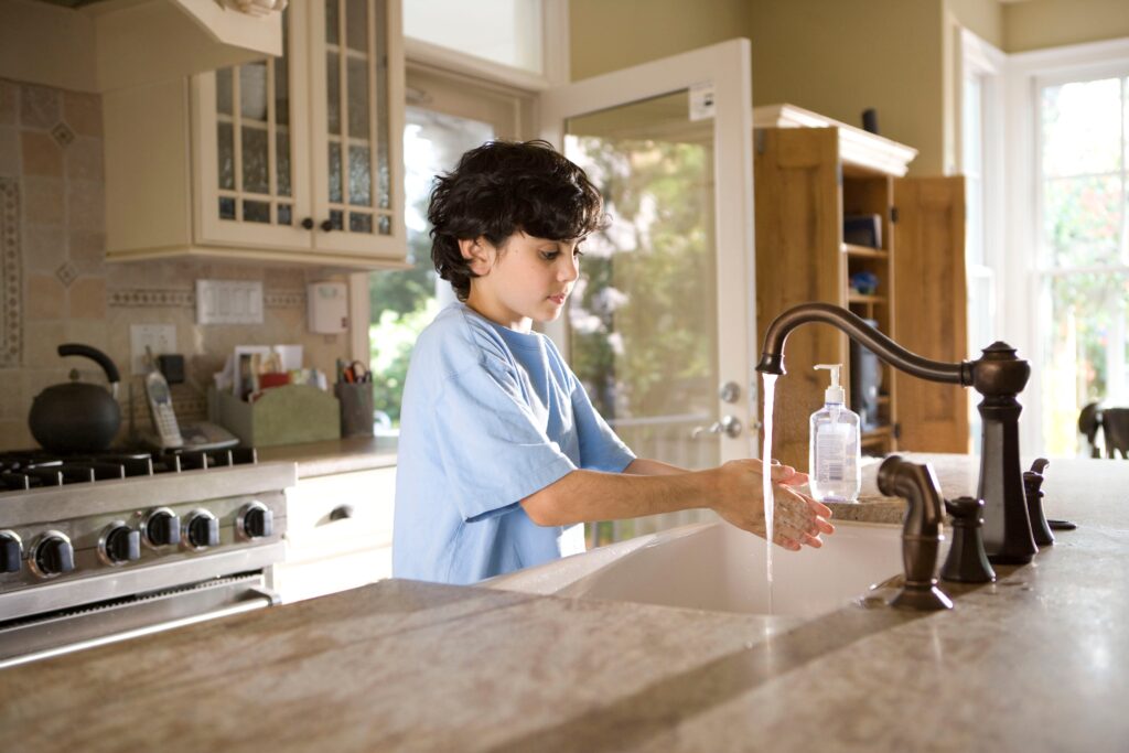 Young child washing hands in the kitchen sink, using soap, showing great knowledge of personal hygiene.