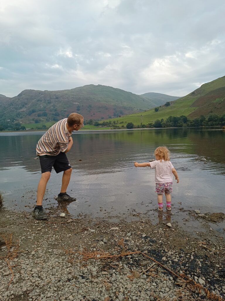 Dad and daughter skimming stones in lake district.