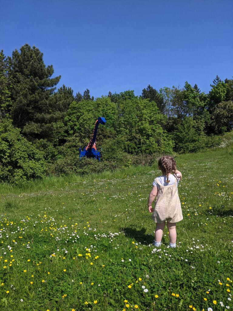 Small girl looking onto steel sculpture of a Brachiosaurus.