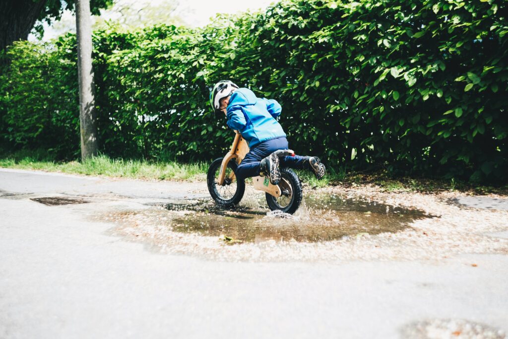 Boy lifting legs up as be bikes through a puddle. This is to go alongside a blog post discussing how to embrace failure with yout child.
