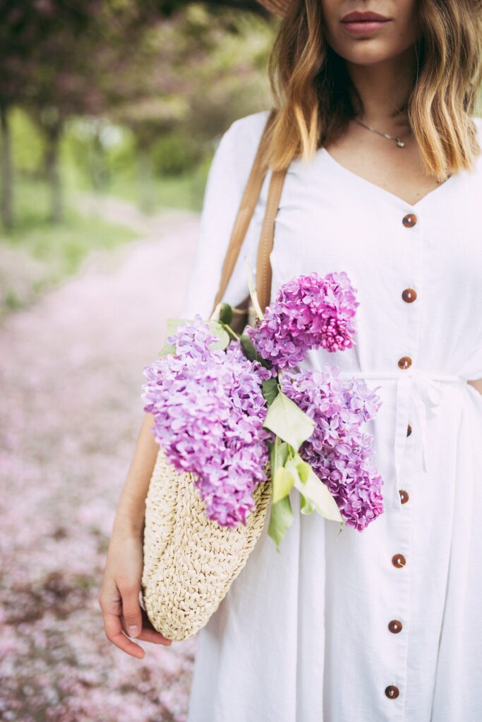Purple flowers in the bag of a white woman wearing a white spring capsule wardrobe dress.