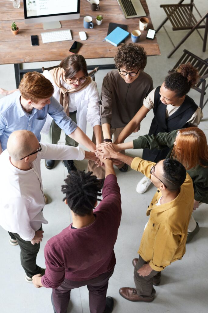 Team members at work putting hands in to high five each other. This is to go with an article discussing ways to build engagement in your workplace and boost team morale.