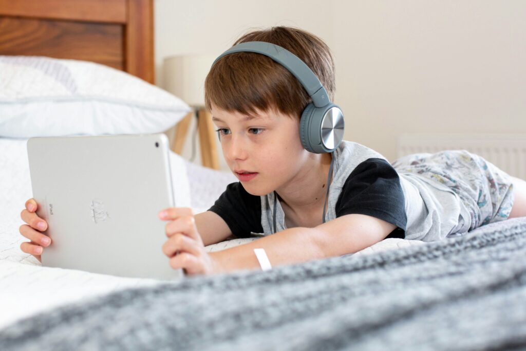Child sitting on bed with tablet and headphones. This is to go with an article giving tips for online saftey.