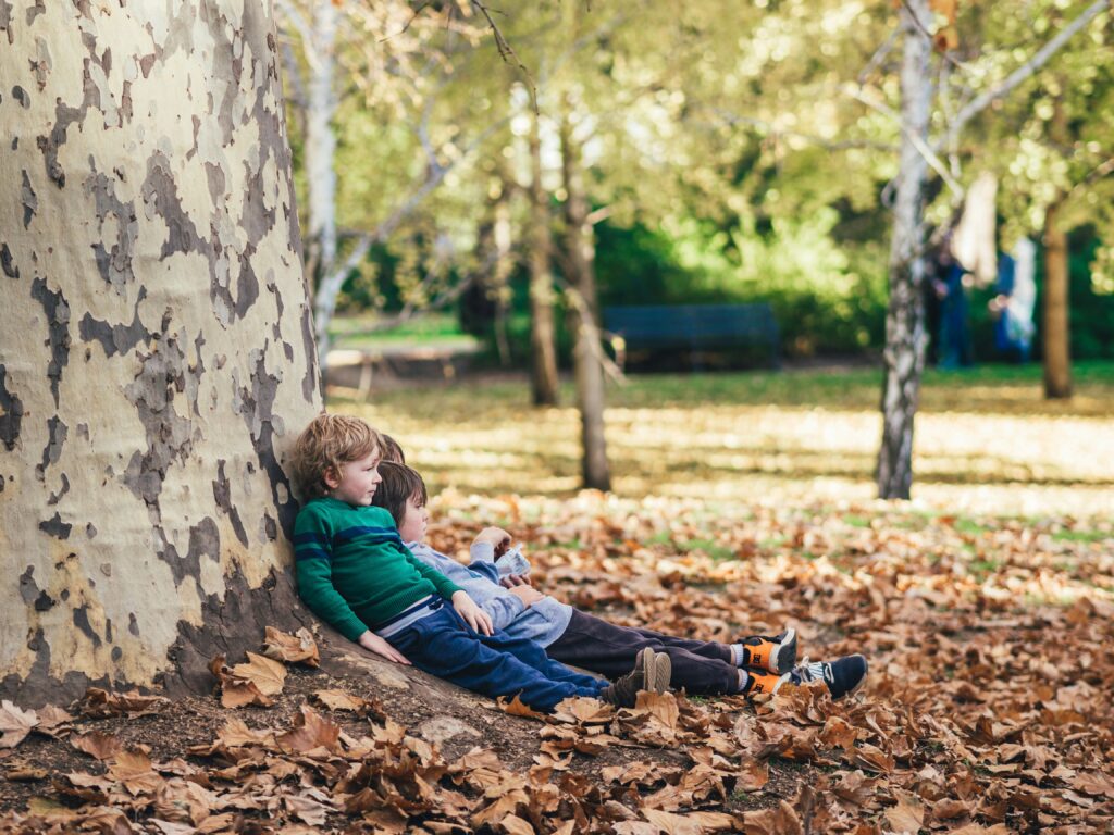 Children sitting down beside a tree in a wraparound care setting.