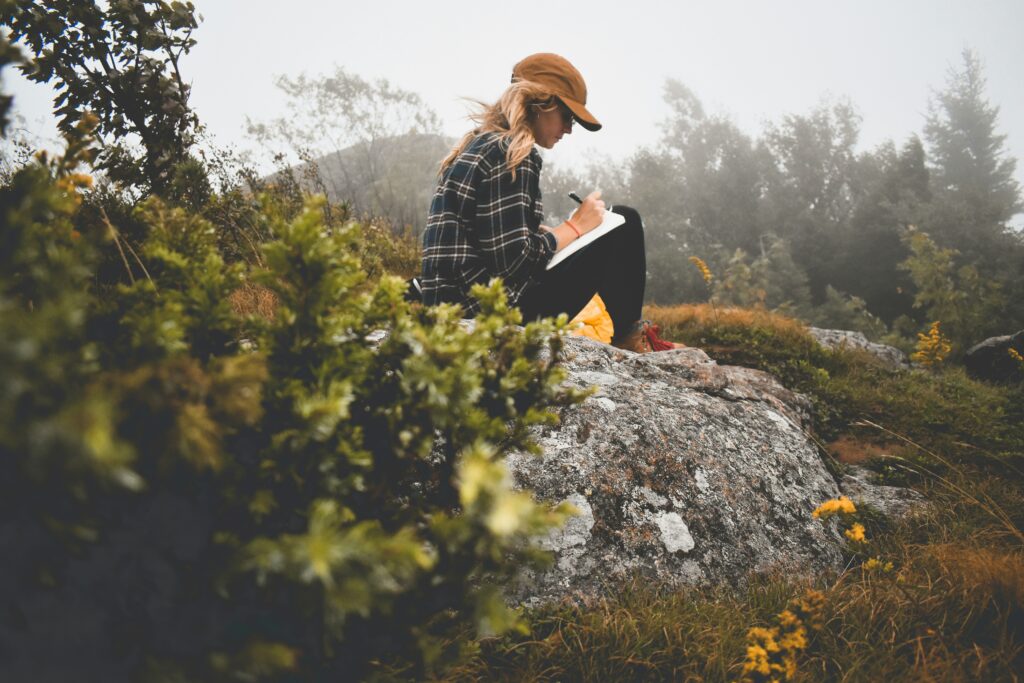 Woman in cap and plaid shirt journaling in the countryside.