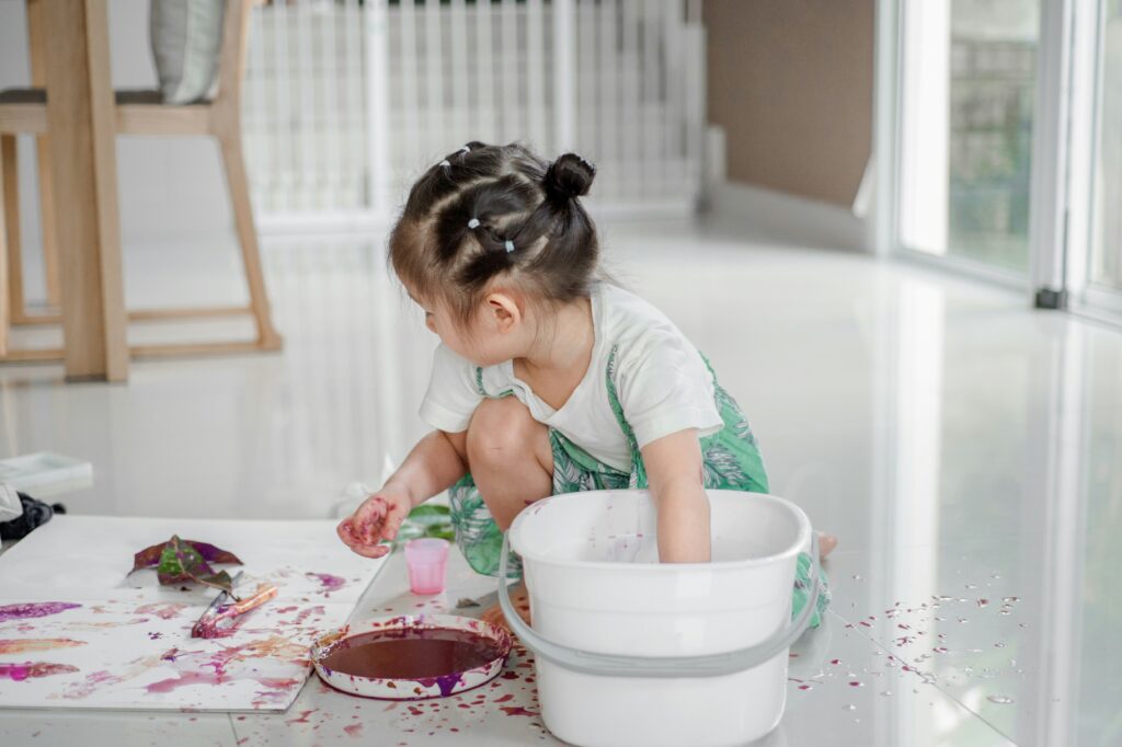 Young girl exploring the benefits of arts and crafts as she paints on the floor.