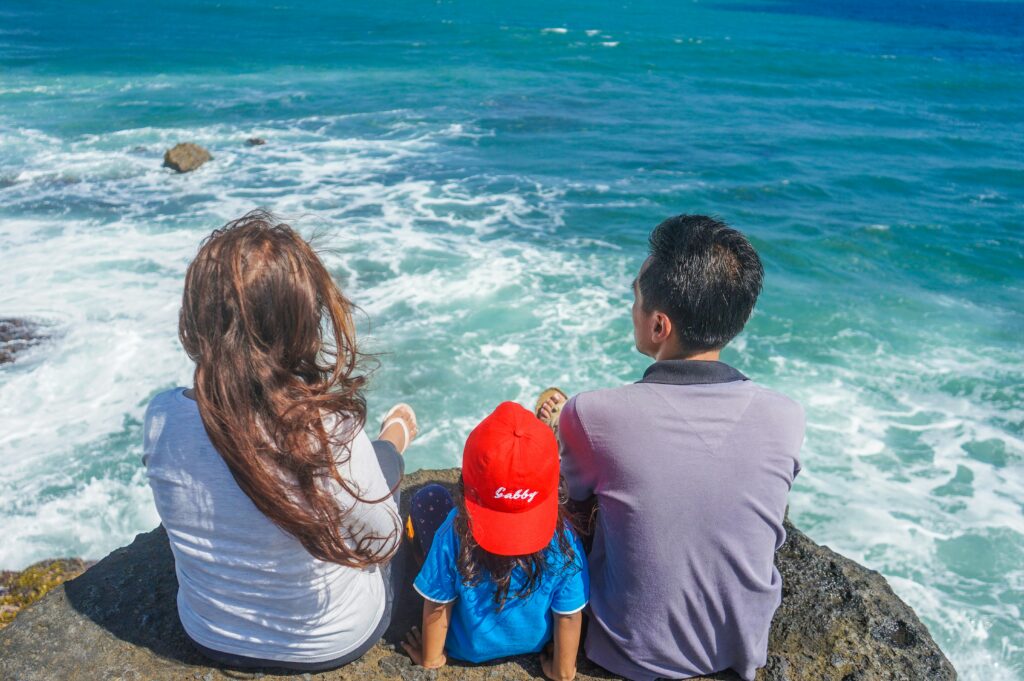 Backshot of family sat on a rock overlooking the sea.