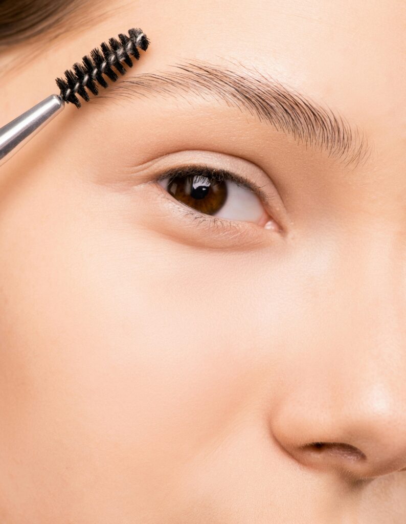 Woman holding up a spoolie to her eyebrow, this is before going in with an eyebrow stamp.