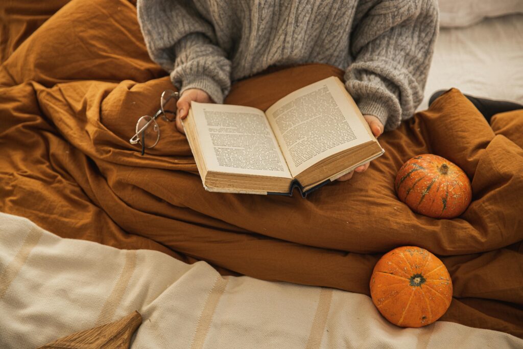 Cosy image of woman wrapped up in mustard coloured throw surrounded by pumpkins This is to go with an article discussing 6 halloween themed bedroom ideas.