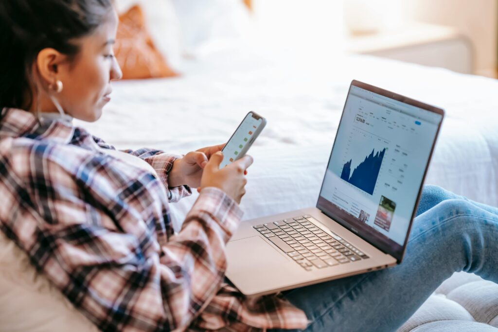 Woman on phone and laptop. Looking at investing.