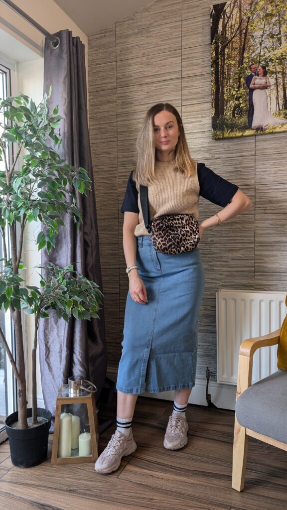 Denim mid skirt styled casually with a sweater vest and trainers.