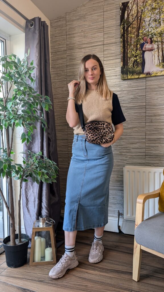Denim mid skirt styled casually with a sweater vest and trainers.