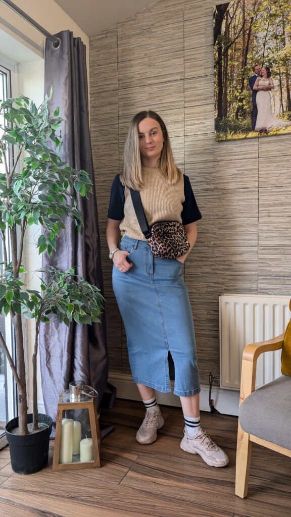 Denim mid skirt styled casually with a sweater vest and trainers.