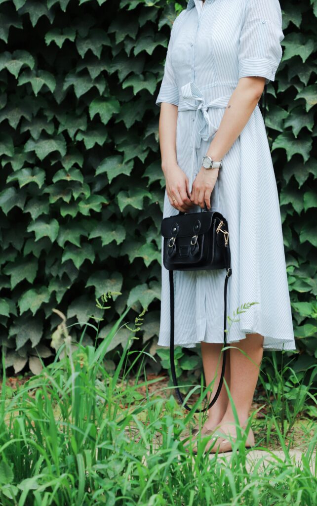 Woman wearing a blue striped midi dress with black satchel bag.