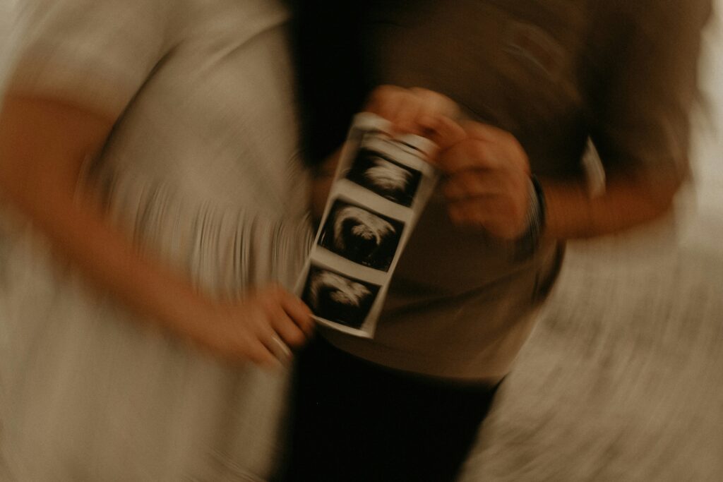 Out of focus image of a couple holding up a baby scan photo, beginning their journey of starting a family.