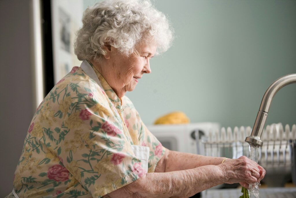 Assisted living. Elderly woman in kitchen using the sink.