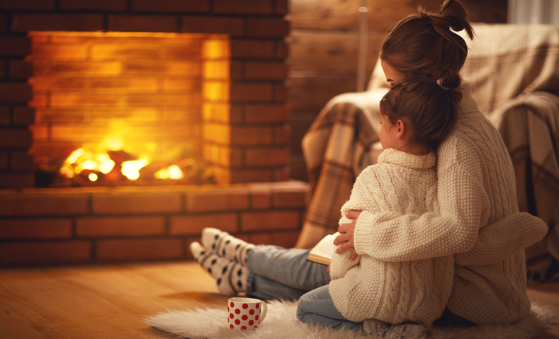 Parent and child sat in front of a fire. This is to go with an article discussing how to keep your house warm.
