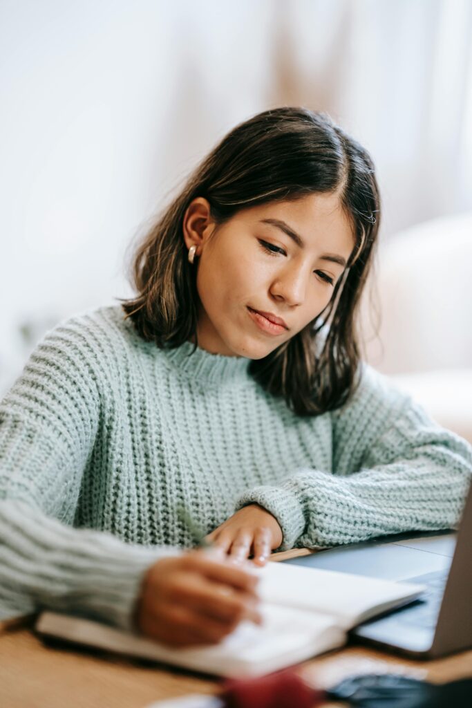 Teenage girl at laptop with a notebook.