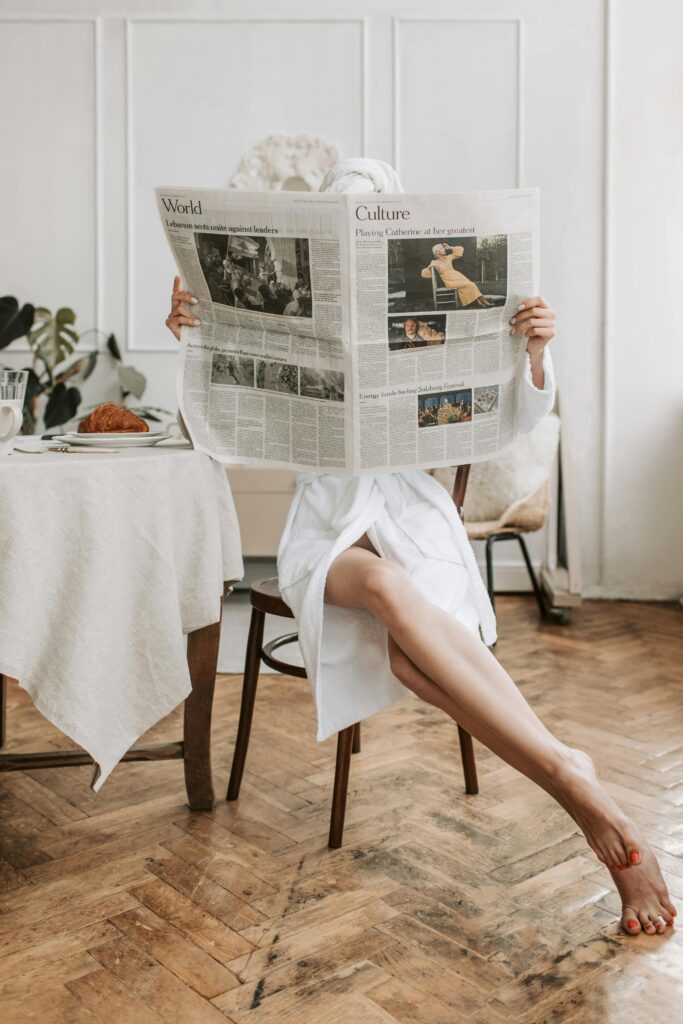 Woman sat at a table with a dressing gown on reading the newspaper. This is to go with an article discussing creative ways to mix up your daily routine.