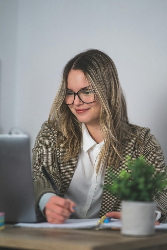 Woman sat at a desk wearing glasses and a checkered blazer.