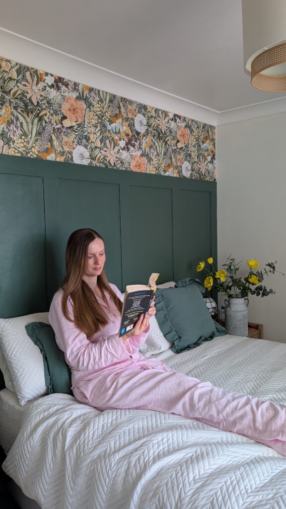 Claire Mac reading in bed wearing British Boxers pink striped pyjamas.