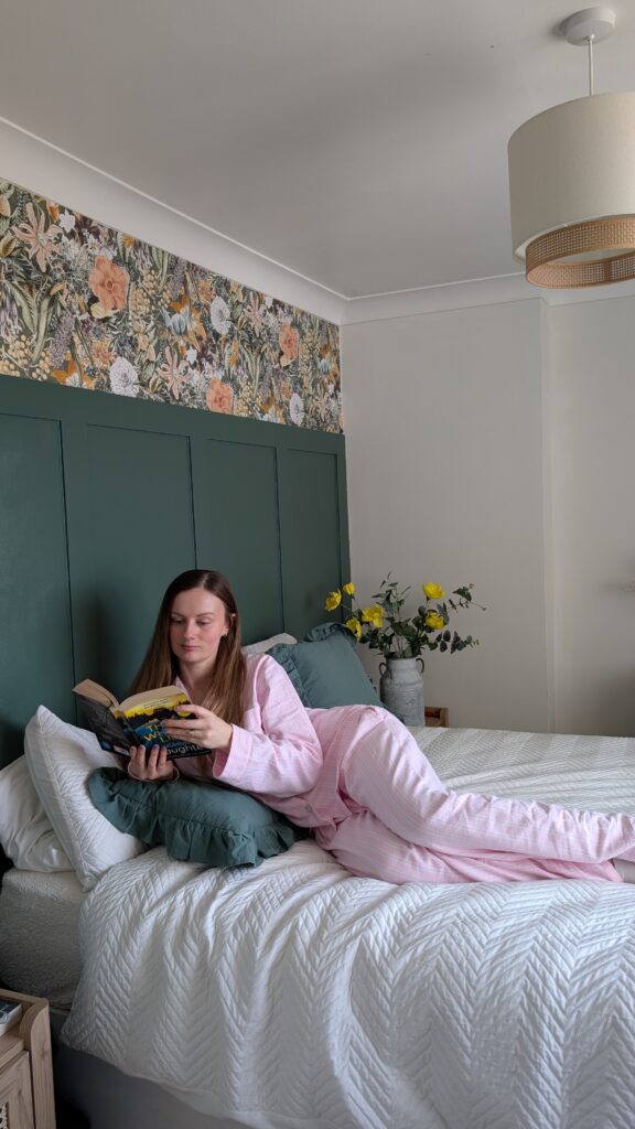 Claire Mac reading in bed wearing British Boxers pink striped pyjamas.