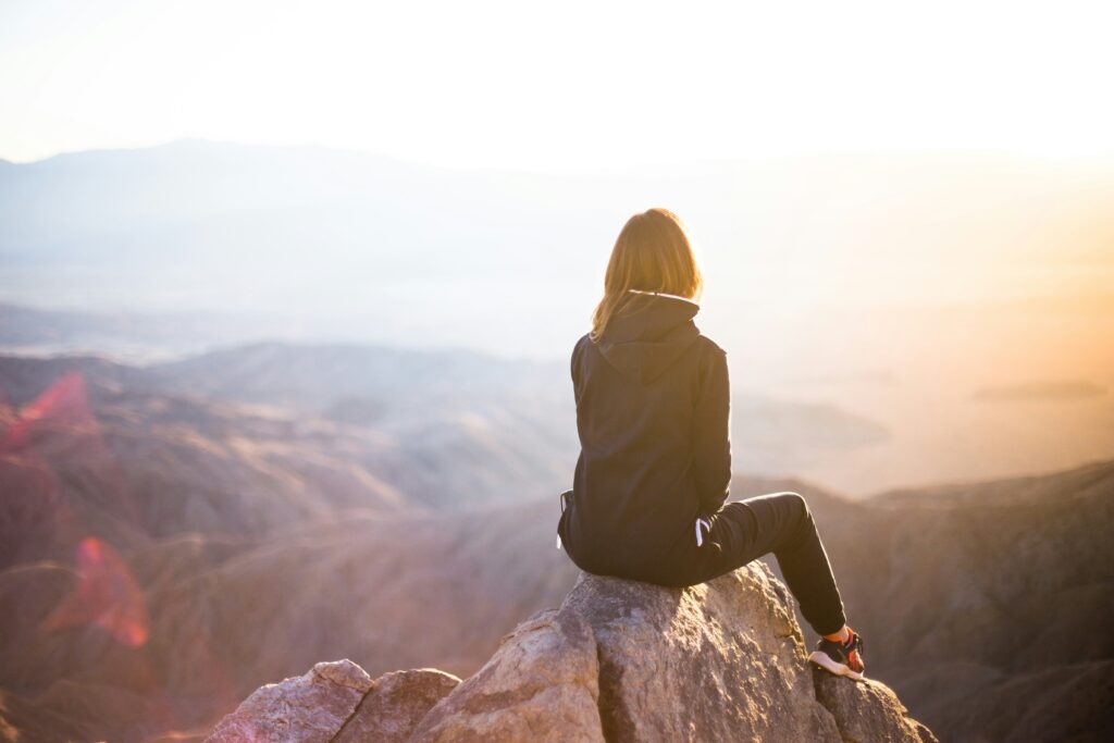 Woman sat at the top of a mountain overlooking the view. This is to go with an article about ways to look after your mental health.