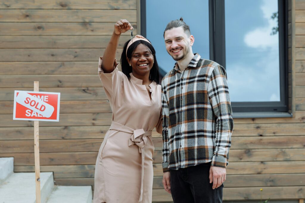 Couple standing outside of their new home holding up keys.
