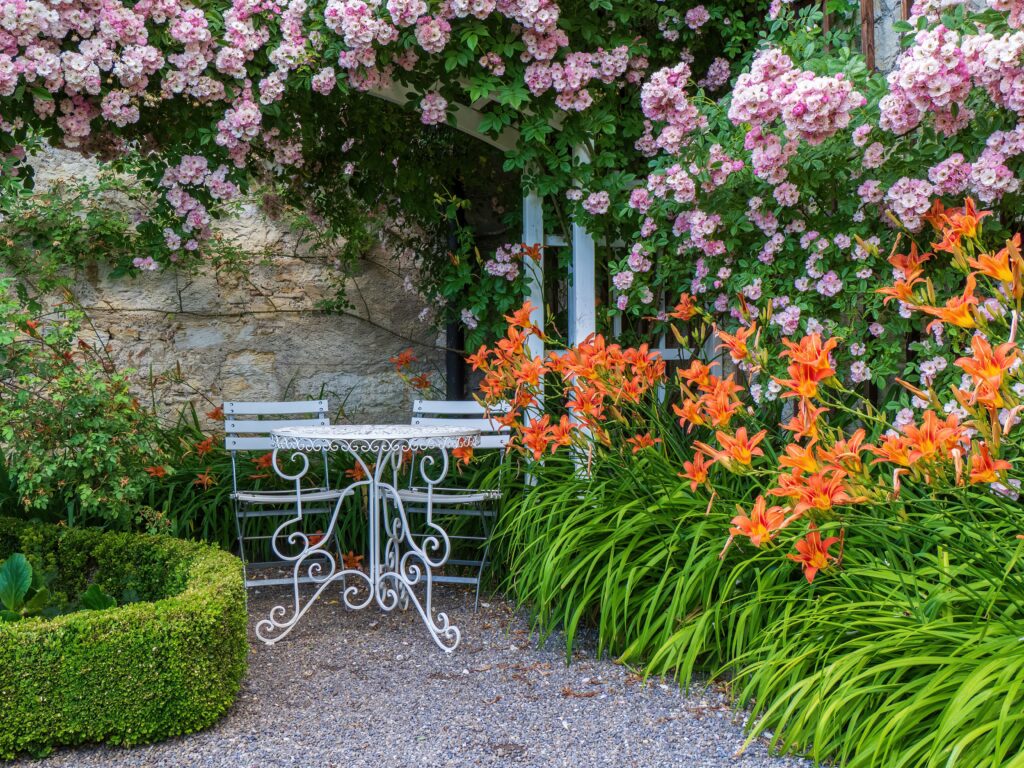 Gravel garden surface with blooming flowers and a white table and chairs.