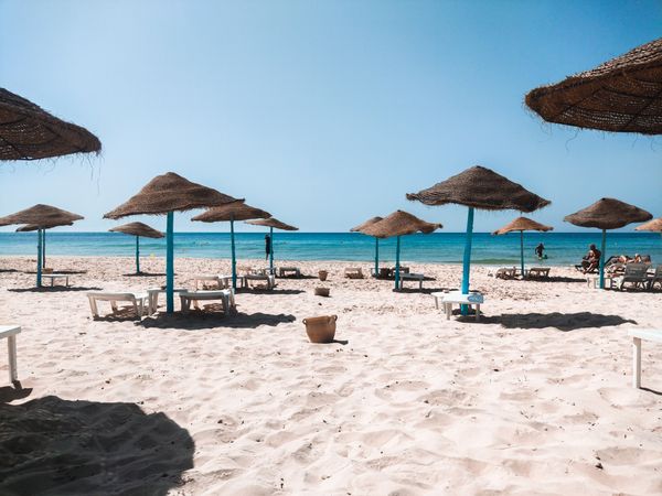 Peaceful sandy beach with straw umbrellas and clear blue sea under a bright sky.